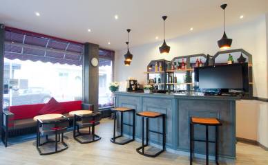 Bar de l'Hôtel Les Pins avec le bar à droite et une porte à gauche. Un canapé et des chaises sont situés à gauche du bar.