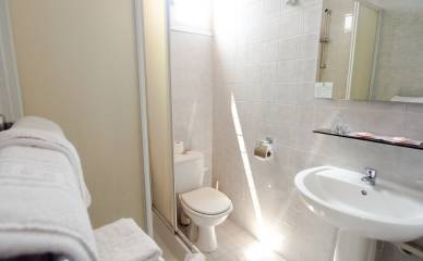 Salle de bain de l'Hôtel Les Pins avec un lavabo et un miroir à droite, ainsi qu'une toilette et une douche à gauche